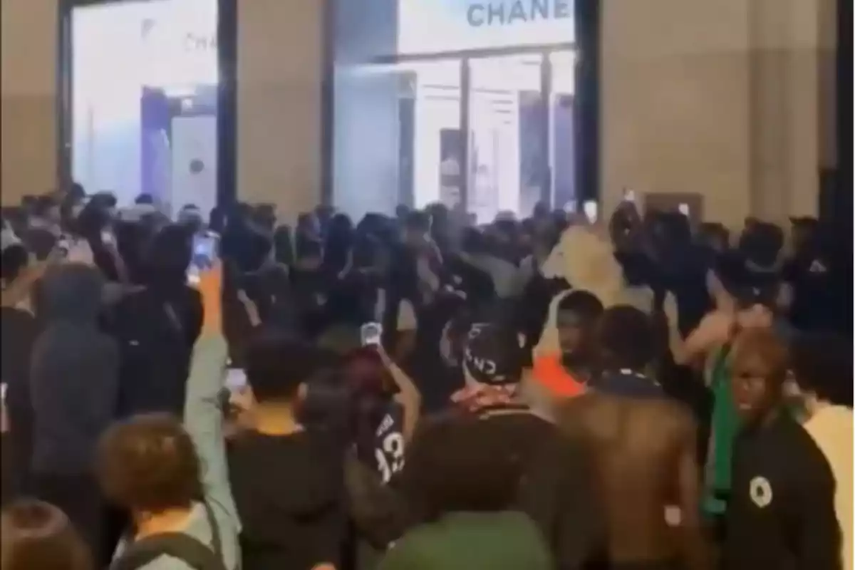 Multitud de personas reunidas frente a una tienda de lujo con letrero visible mientras varias personas graban la escena con sus teléfonos móviles Multitud de personas reunidas frente a una tienda de lujo con letrero visible mientras varias personas graban la escena con sus teléfonos móviles
