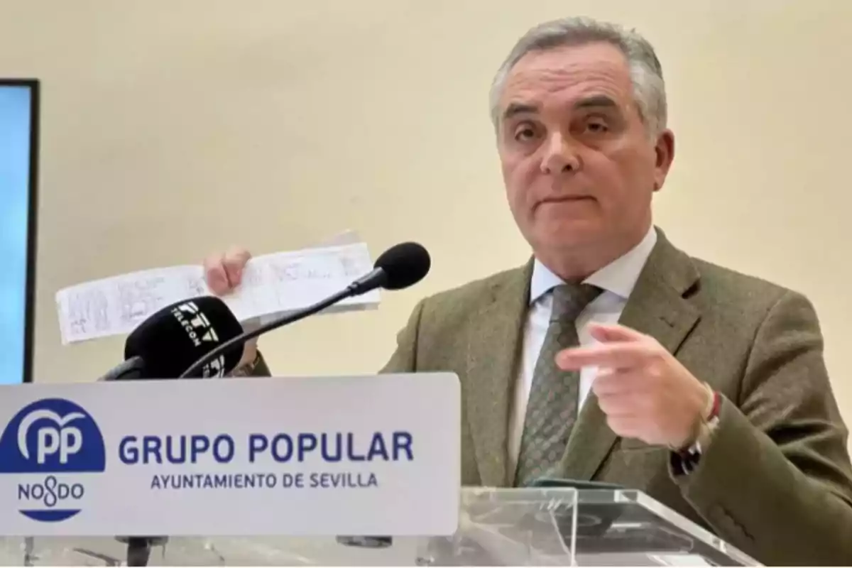 Un hombre de traje habla en una rueda de prensa del Grupo Popular del Ayuntamiento de Sevilla mientras sostiene un documento en la mano. Un hombre de traje habla en una rueda de prensa del Grupo Popular del Ayuntamiento de Sevilla mientras sostiene un documento en la mano.