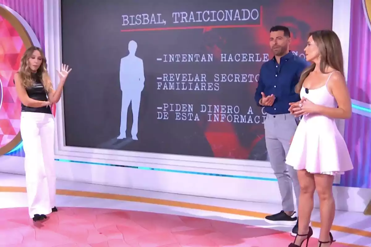Tres personas están de pie en un set de 'Socialité' frente a una pantalla que muestra texto sobre una figura anónima y menciona temas de traición y secretos familiares. Tres personas están de pie en un set de 'Socialité' frente a una pantalla que muestra texto sobre una figura anónima y menciona temas de traición y secretos familiares.