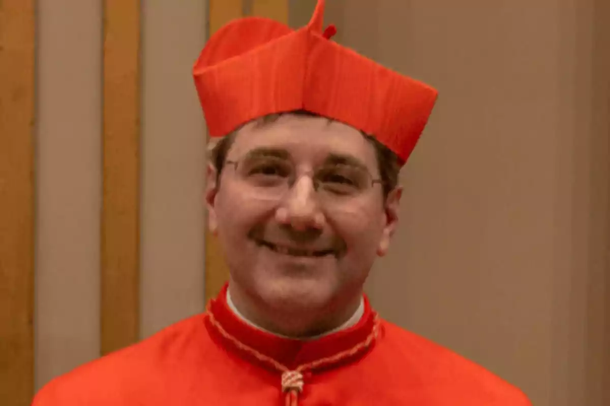 A man in red clothing and hat smiles in front of a neutral background. A man in red clothing and hat smiles in front of a neutral background.
