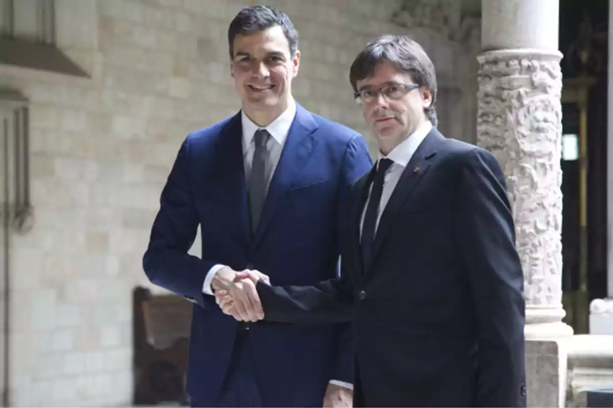 Dos hombres de traje estrechando manos en un entorno arquitectónico histórico.