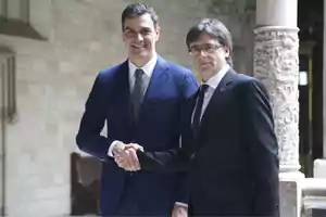 Dos hombres de traje estrechando manos en un entorno arquitectónico histórico.