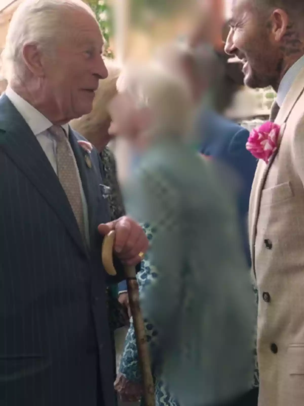 Dos hombres conversan sonrientes en un evento formal, uno lleva un bastón y el otro una flor en la solapa. Dos hombres conversan sonrientes en un evento formal, uno lleva un bastón y el otro una flor en la solapa.