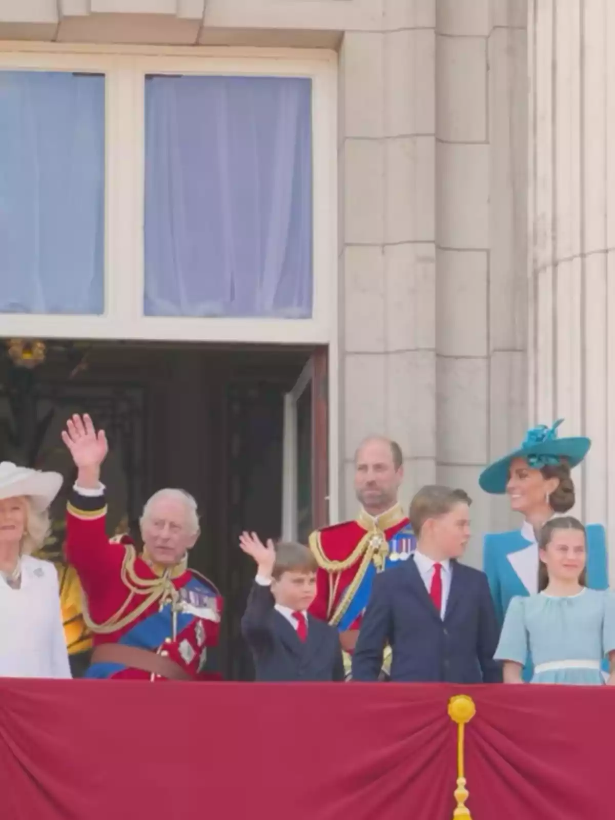 Grupo de personas vestidas de manera formal saludando desde un balcón decorado con una tela roja Grupo de personas vestidas de manera formal saludando desde un balcón decorado con una tela roja
