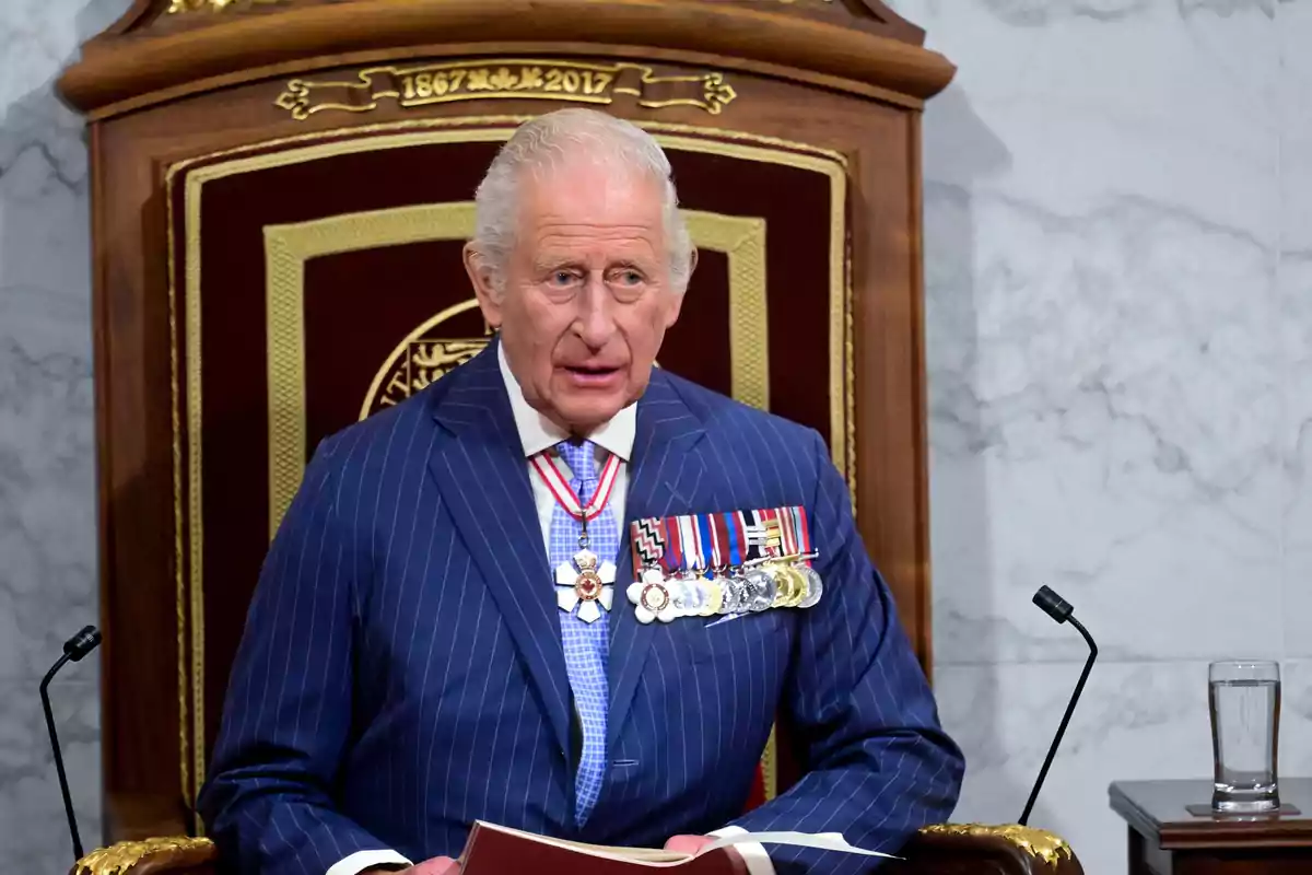 Carlos III vestido con traje azul a rayas y condecoraciones sentado en un trono de madera decorado con detalles dorados Carlos III vestido con traje azul a rayas y condecoraciones sentado en un trono de madera decorado con detalles dorados
