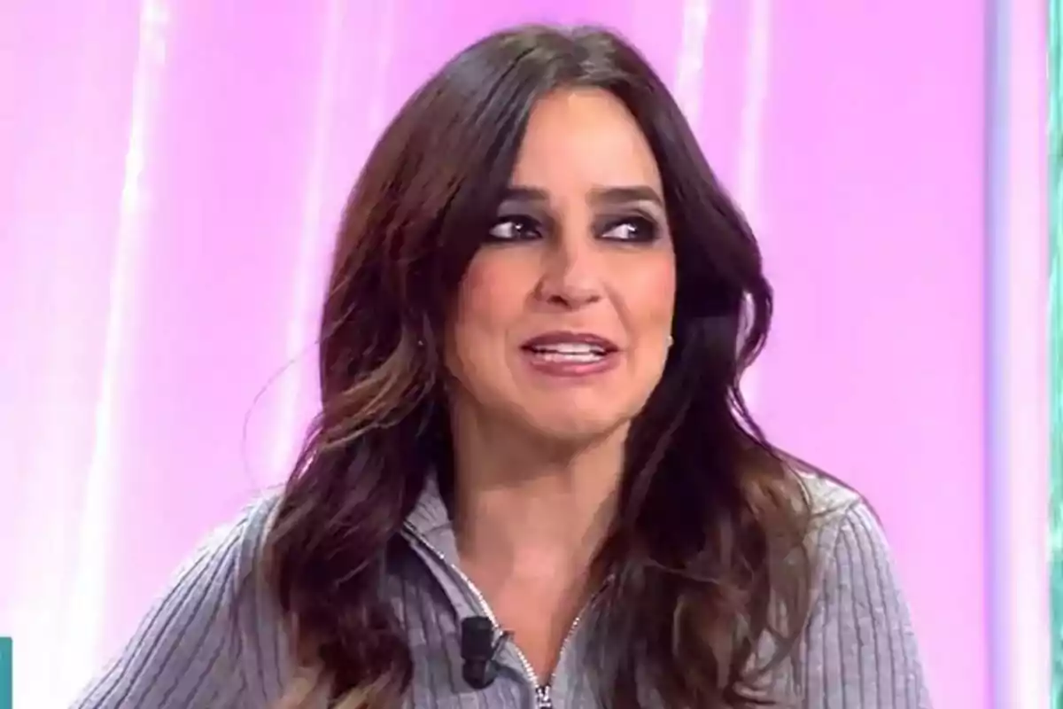 Carmen Alcayde con cabello oscuro y suelto, vestida con un suéter gris, sonríe mientras está en un entorno con fondo rosa en Fiesta. Carmen Alcayde con cabello oscuro y suelto, vestida con un suéter gris, sonríe mientras está en un entorno con fondo rosa en Fiesta.
