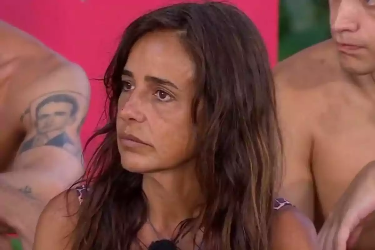 Carmen Alcayde con cabello largo y oscuro mira hacia un lado mientras está rodeada de otras personas en un entorno al aire libre. Carmen Alcayde con cabello largo y oscuro mira hacia un lado mientras está rodeada de otras personas en un entorno al aire libre.