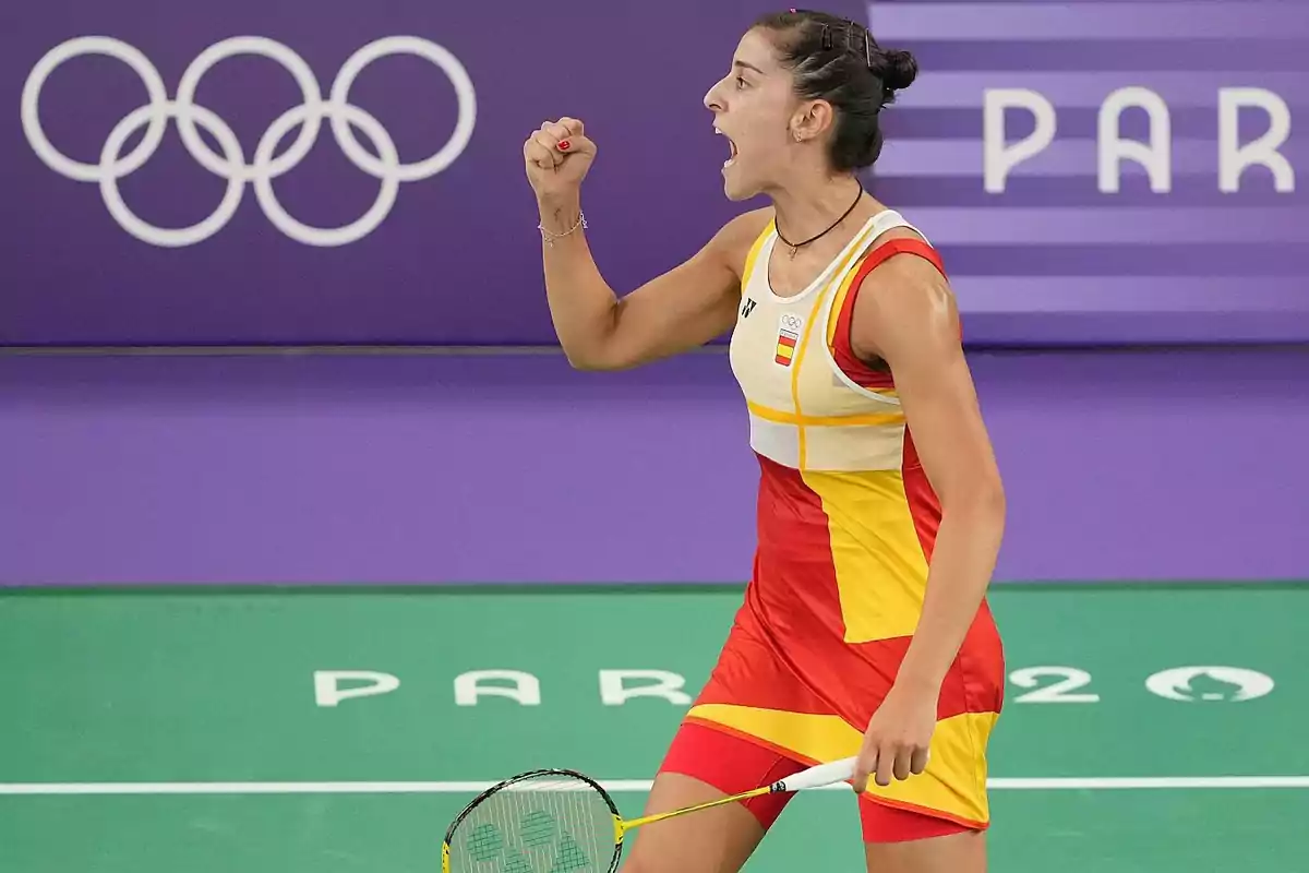 Jugadora de bádminton celebrando durante un partido en los Juegos Olímpicos, con el logo olímpico y la palabra "PARIS" en el fondo.