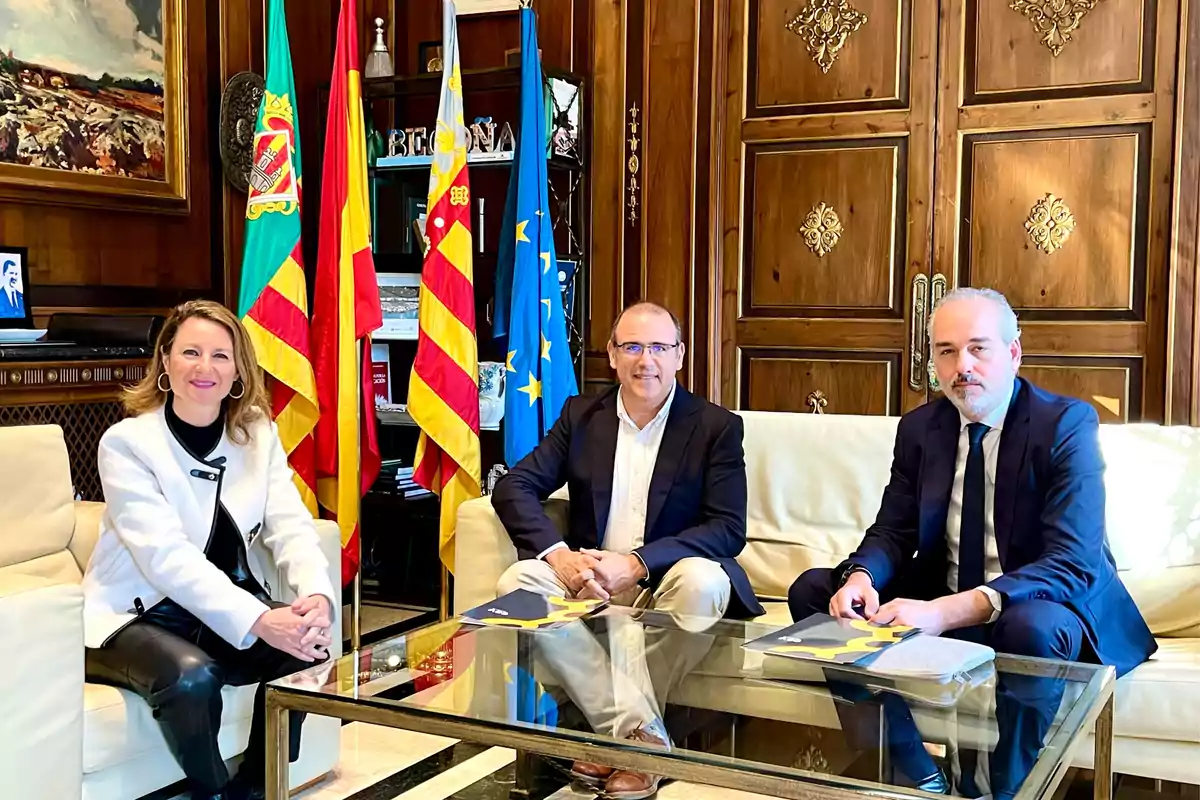 Three people sitting on a white sofa in a room with flags and a glass table.