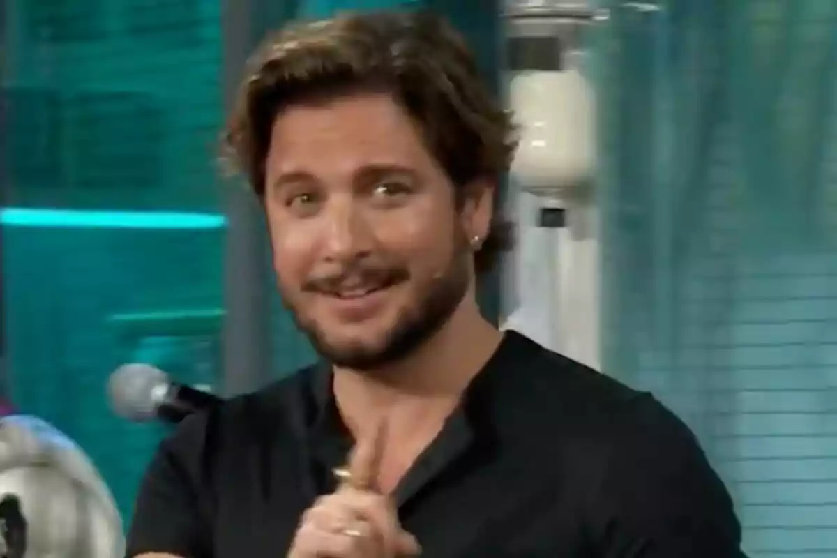 Manuel Carrasco con barba y cabello castaño sonríe mientras señala con el dedo en un entorno interior con luces azules en 'La Revuelta'. Manuel Carrasco con barba y cabello castaño sonríe mientras señala con el dedo en un entorno interior con luces azules en 'La Revuelta'.