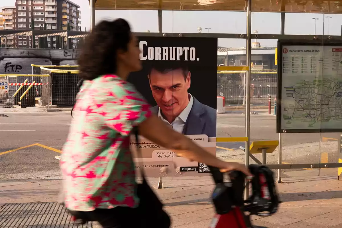 Una mujer pasa en bicicleta frente a una parada de autobús donde hay un cartel con la palabra Una mujer pasa en bicicleta frente a una parada de autobús donde hay un cartel con la palabra