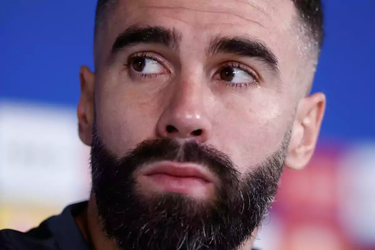 Primer plano de un hombre con barba y cabello corto mirando hacia un lado.