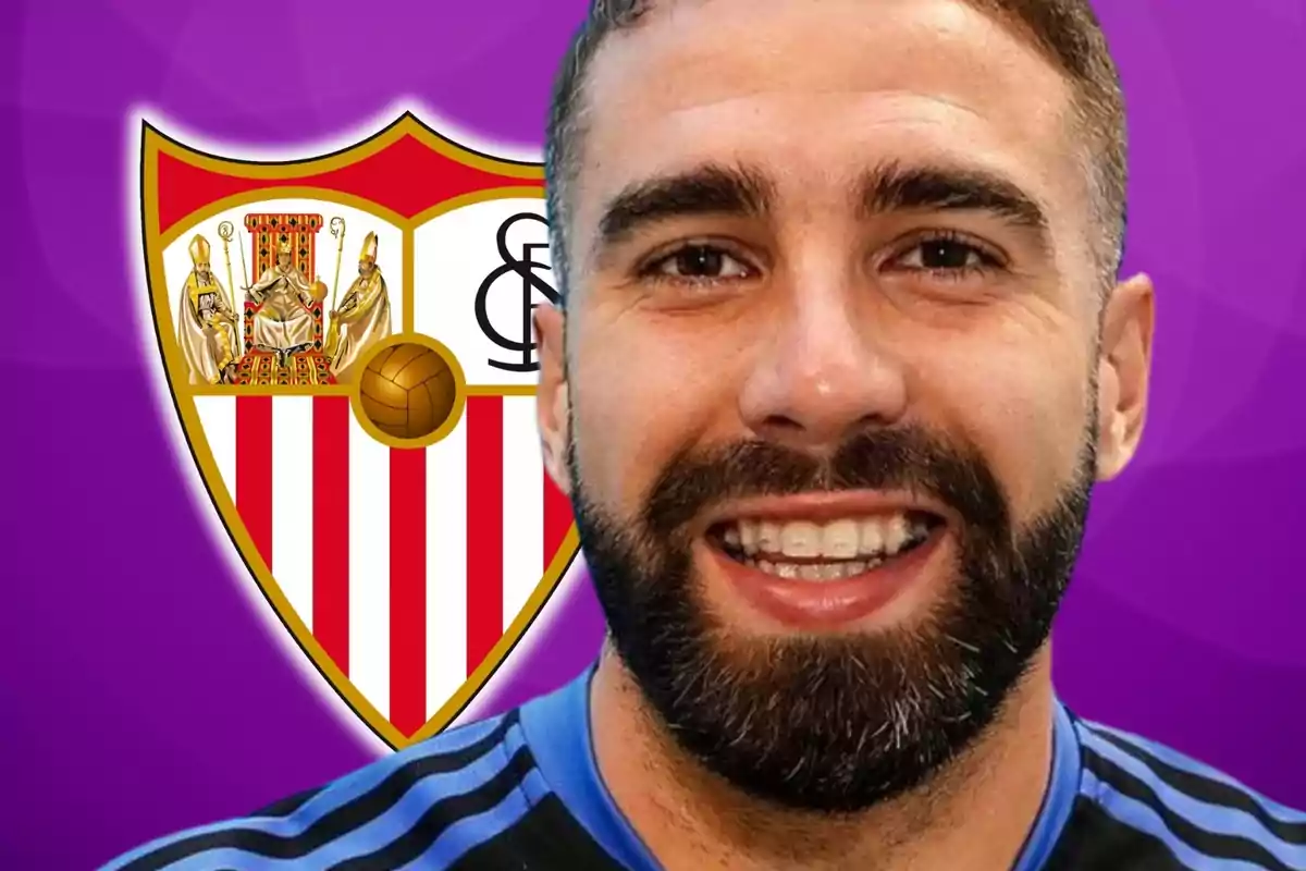 Un hombre sonriente con barba frente al escudo del Sevilla FC sobre un fondo morado.