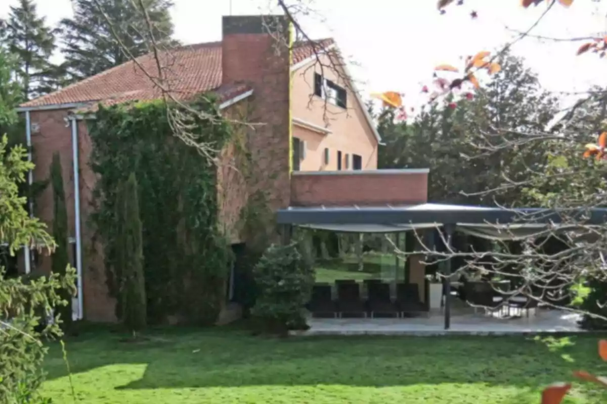 Casa de ladrillo con techo a dos aguas rodeada de vegetación y un jardín amplio con terraza cubierta Casa de ladrillo con techo a dos aguas rodeada de vegetación y un jardín amplio con terraza cubierta