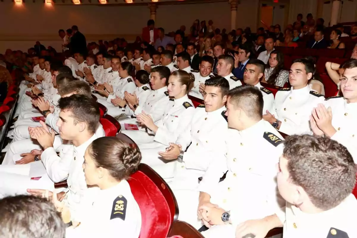 Grupo de cadetes vestidos con uniformes blancos sentados en un auditorio aplaudiendo durante un evento formal Grupo de cadetes vestidos con uniformes blancos sentados en un auditorio aplaudiendo durante un evento formal