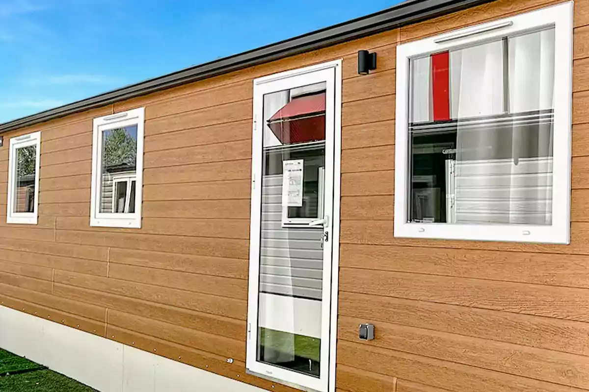 Una casa móvil con revestimiento de madera, ventanas y una puerta blanca.