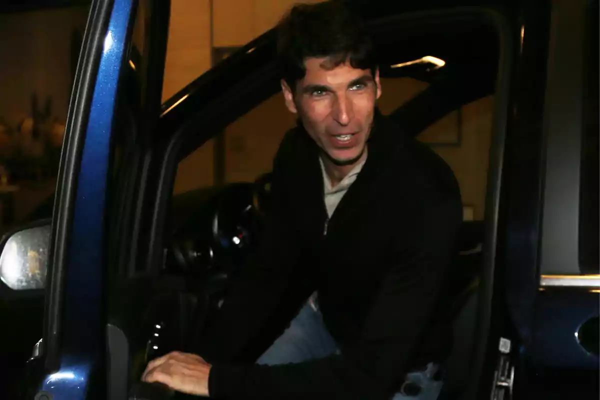 Un hombre con suéter negro está saliendo de un automóvil azul oscuro en un entorno interior. Un hombre con suéter negro está saliendo de un automóvil azul oscuro en un entorno interior.