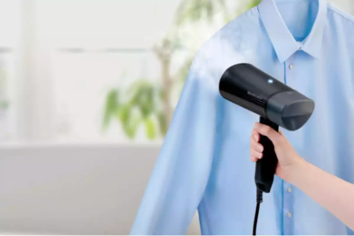 Persona usando un vaporizador de mano para quitar arrugas de una camisa azul Persona usando un vaporizador de mano para quitar arrugas de una camisa azul