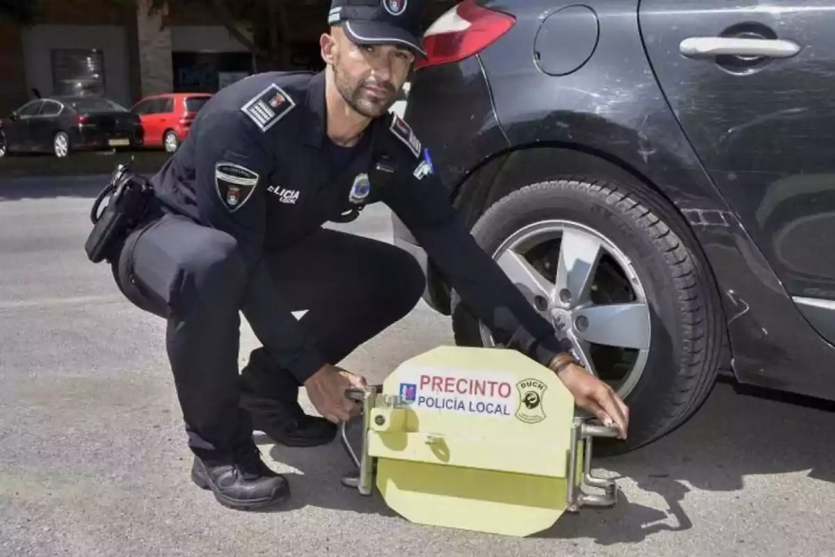 Un oficial de policía local coloca un inmovilizador de vehículos en la rueda de un automóvil.