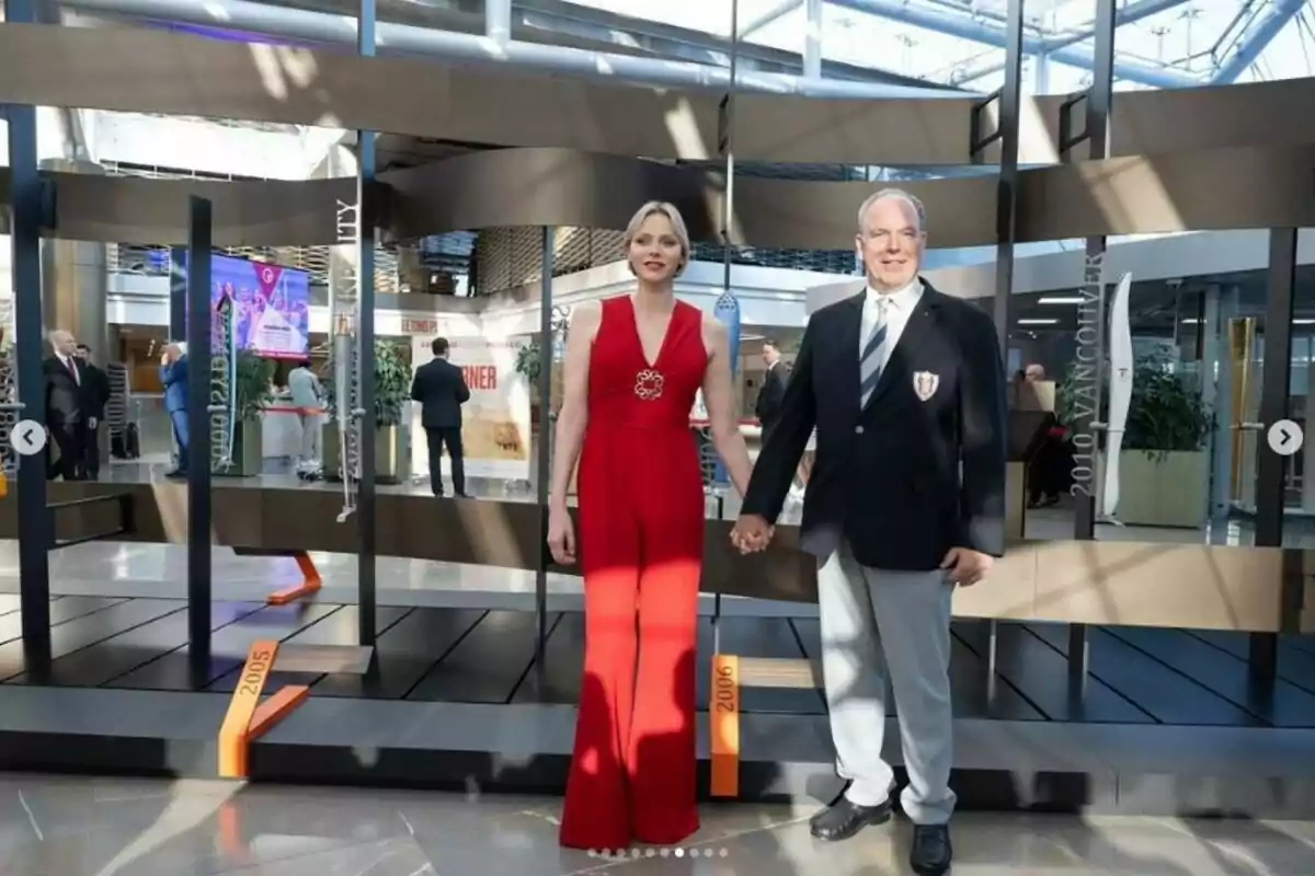 Charlene y Alberto de Mónaco posando de la mano en un evento, ella lleva un vestido rojo y él un traje con corbata, en un entorno moderno con varias personas al fondo. Post del principado de Mónaco en Instagram el 19 de julio de 2024 Charlene y Alberto de Mónaco posando de la mano en un evento, ella lleva un vestido rojo y él un traje con corbata, en un entorno moderno con varias personas al fondo. Post del principado de Mónaco en Instagram el 19 de julio de 2024