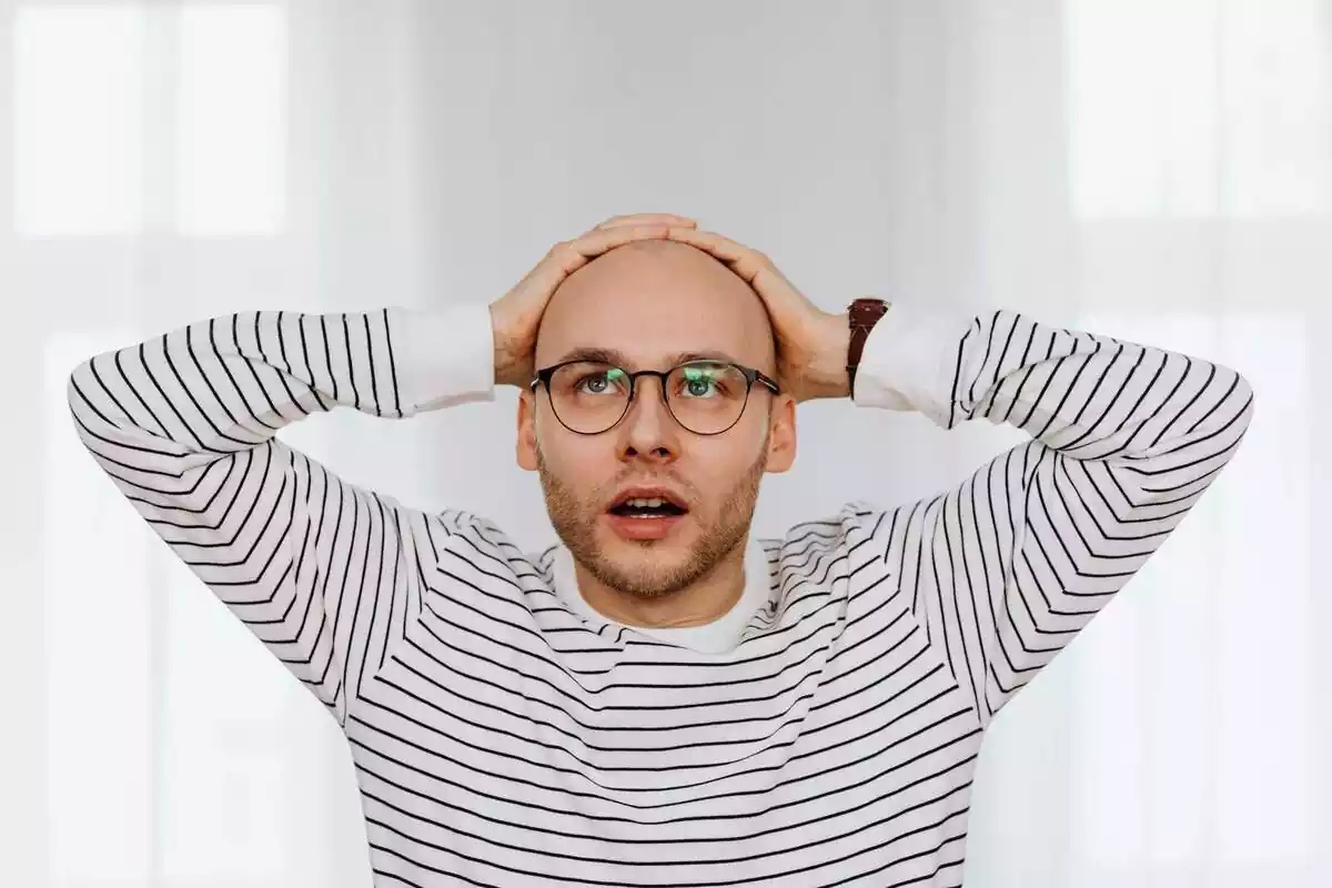 Chico con gafas y sin pelo con las manos en la cabeza