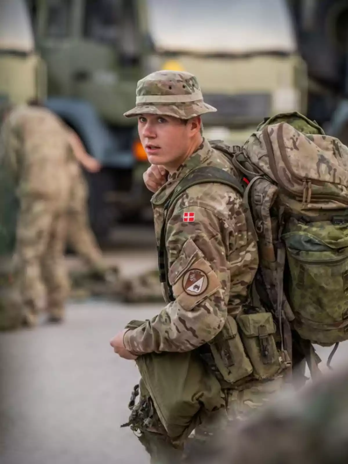 Un soldado con uniforme de camuflaje y mochila grande mira hacia atrás mientras se encuentra en un entorno militar. Un soldado con uniforme de camuflaje y mochila grande mira hacia atrás mientras se encuentra en un entorno militar.