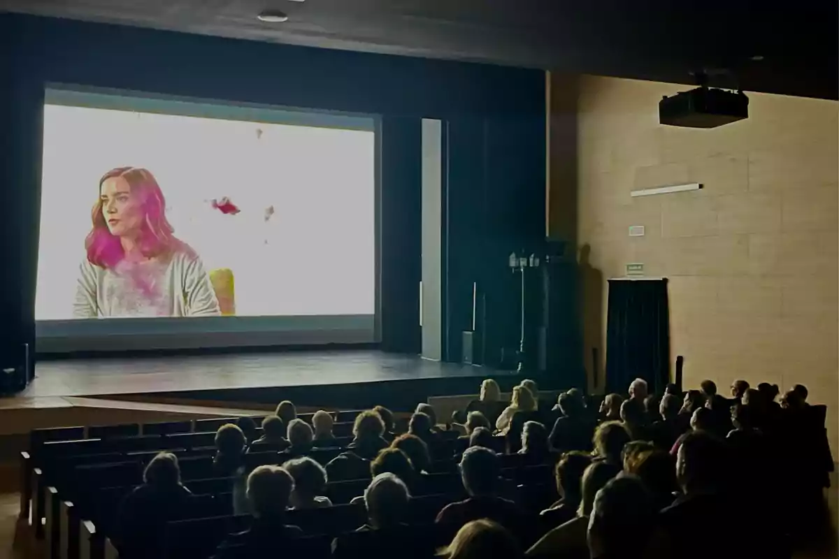 People sitting in an auditorium watching a movie projected on a big screen.