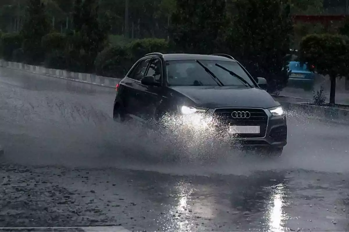 Un coche oscuro atravesando un charco de agua en medio de una tormenta Un coche oscuro atravesando un charco de agua en medio de una tormenta