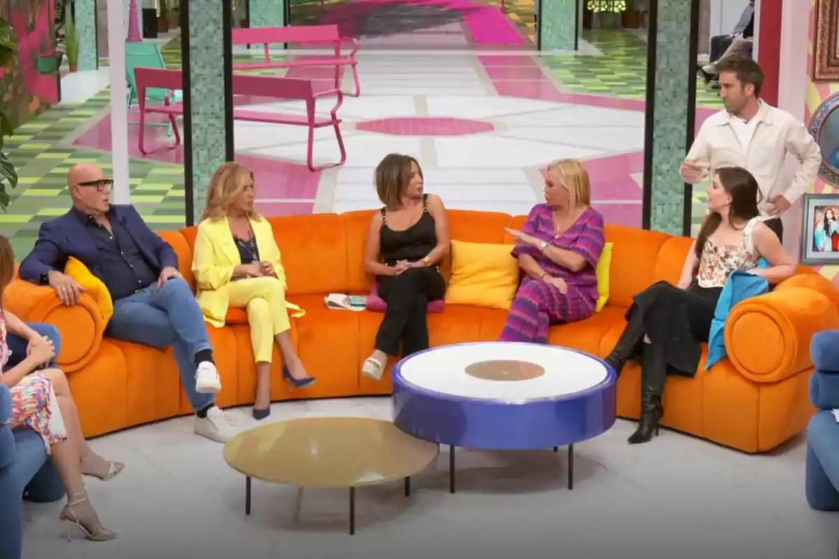 Un grupo de personas formado por Kiko Matamoros, Lydia Lozano, María Patiño, Belén Esteban, Inés Hernand y Aitor Albizua está sentado en un sofá naranja en un set de televisión de La Familia de la Tele colorido, conversando entre ellos mientras un hombre de pie parece estar hablando. Un grupo de personas formado por Kiko Matamoros, Lydia Lozano, María Patiño, Belén Esteban, Inés Hernand y Aitor Albizua está sentado en un sofá naranja en un set de televisión de La Familia de la Tele colorido, conversando entre ellos mientras un hombre de pie parece estar hablando.