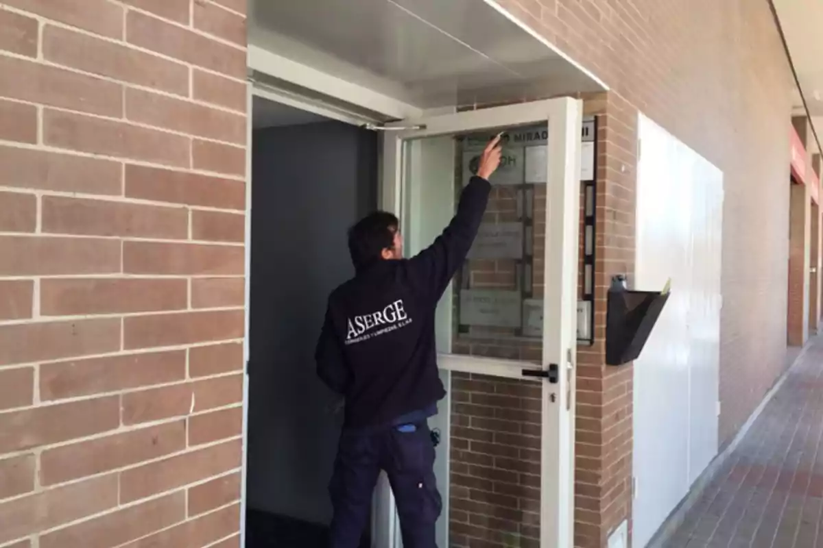 Un conserge de Aserge limpiando una puerta de una comunidad de vecinos
