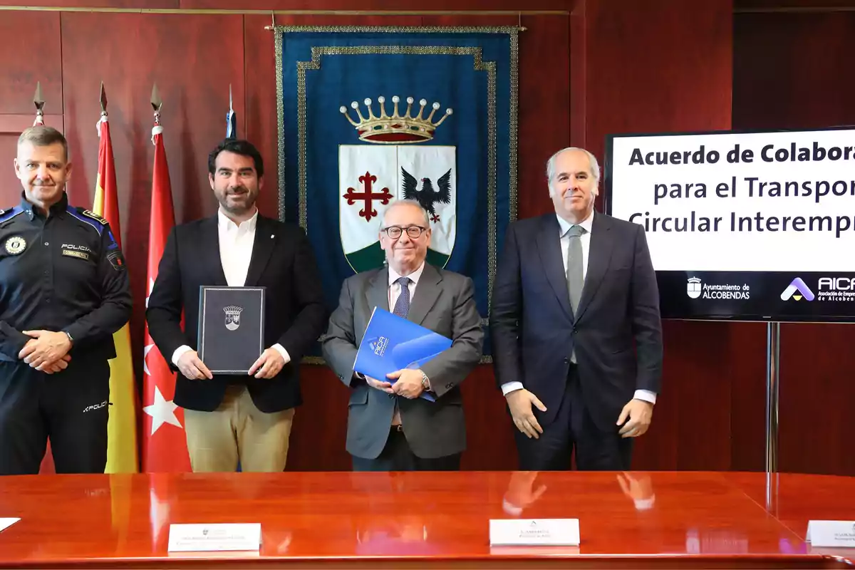 Un grupo de hombres en traje formal posa frente a un estandarte y una pantalla que anuncia un acuerdo de colaboración para el transporte circular interempresarial.