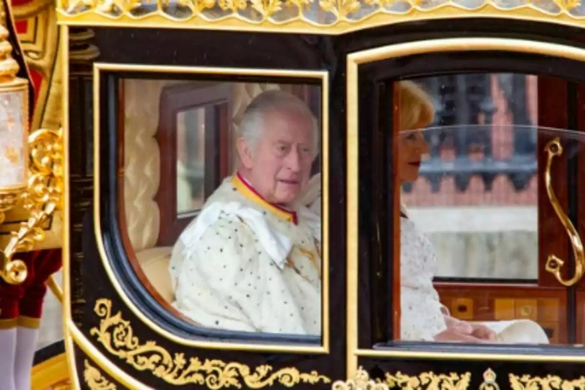 El rey Carlos III y la reina Camilla, elegantemente vestidos, se pasean en una carroza decorada con detalles dorados durante el día de la coronación de él como rey de Inglaterra. El rey Carlos III y la reina Camilla, elegantemente vestidos, se pasean en una carroza decorada con detalles dorados durante el día de la coronación de él como rey de Inglaterra.