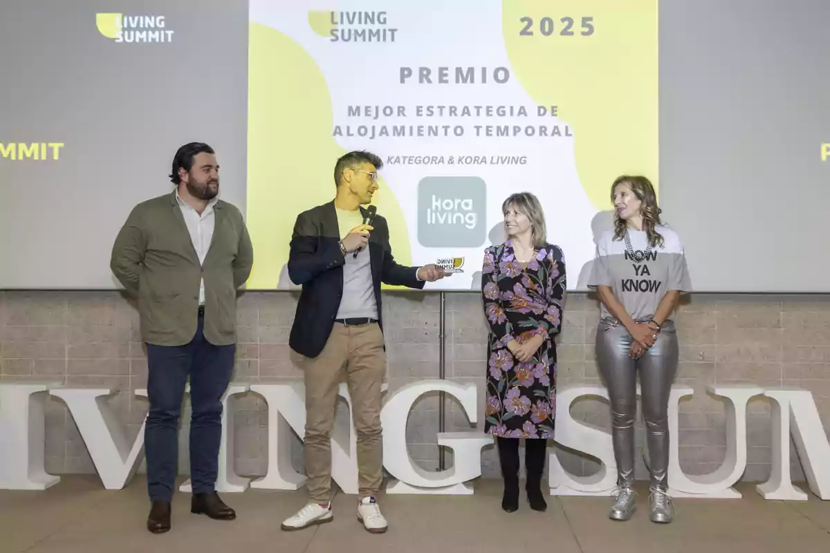 Un grupo de personas está en un escenario recibiendo un premio por la mejor estrategia de alojamiento temporal en un evento llamado Living Summit 2025.