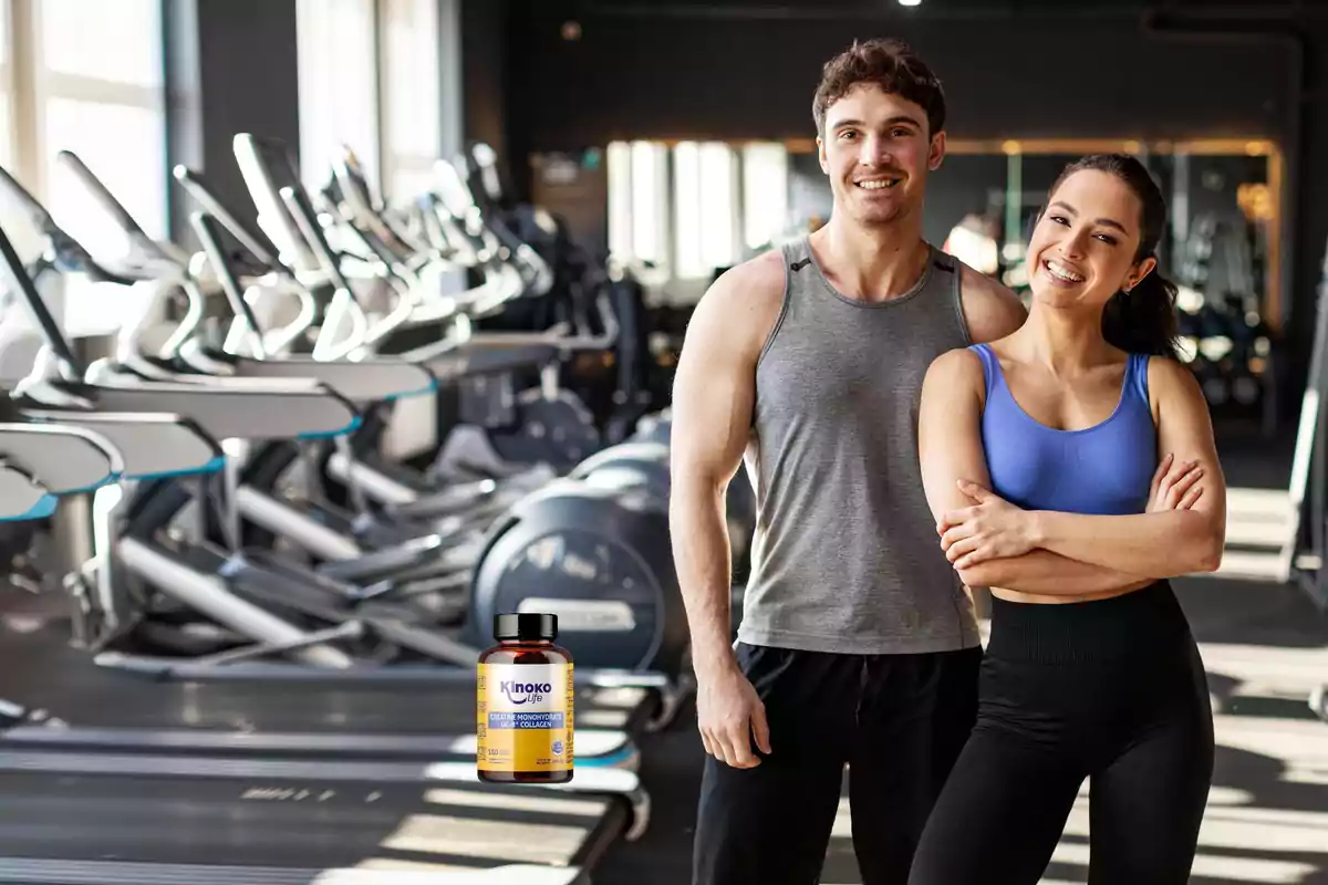 Dos personas en ropa deportiva posan sonrientes en un gimnasio con varias máquinas de ejercicio en el fondo y un frasco de suplemento en la esquina inferior izquierda.