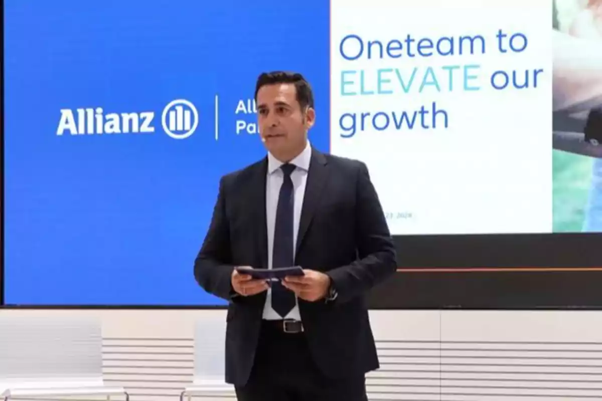 Hombre en traje dando una presentación frente a una pantalla con el logo de Allianz y el texto "Oneteam to ELEVATE our growth".