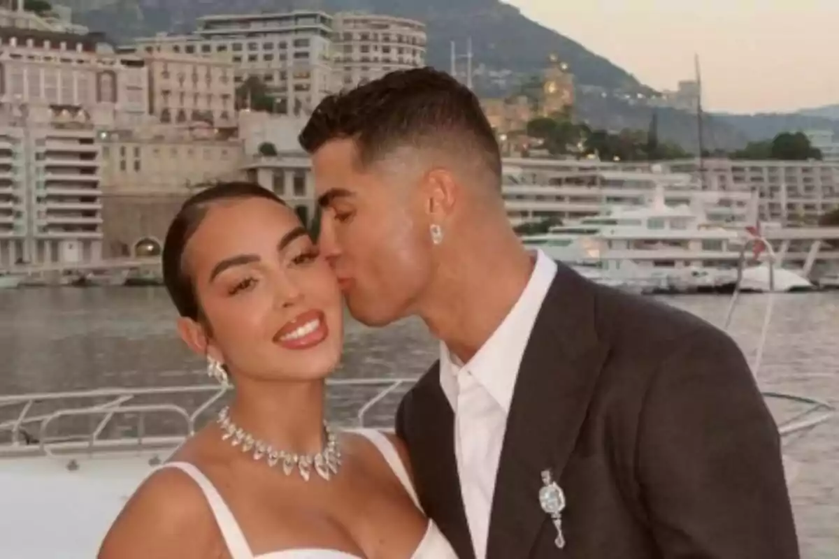 A couple -consisting of Cristiano Ronaldo and Georgina Rodríguez- posing on a yacht with an urban and mountainous landscape in the background. A couple -consisting of Cristiano Ronaldo and Georgina Rodríguez- posing on a yacht with an urban and mountainous landscape in the background.