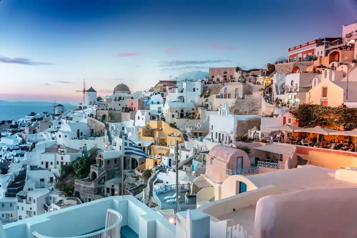 Vista panorámica de un pintoresco pueblo costero con casas blancas y coloridas en una colina al atardecer.