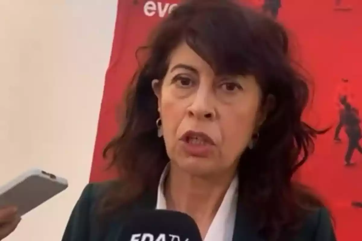 Mujer hablando frente a un micrófono con fondo rojo.