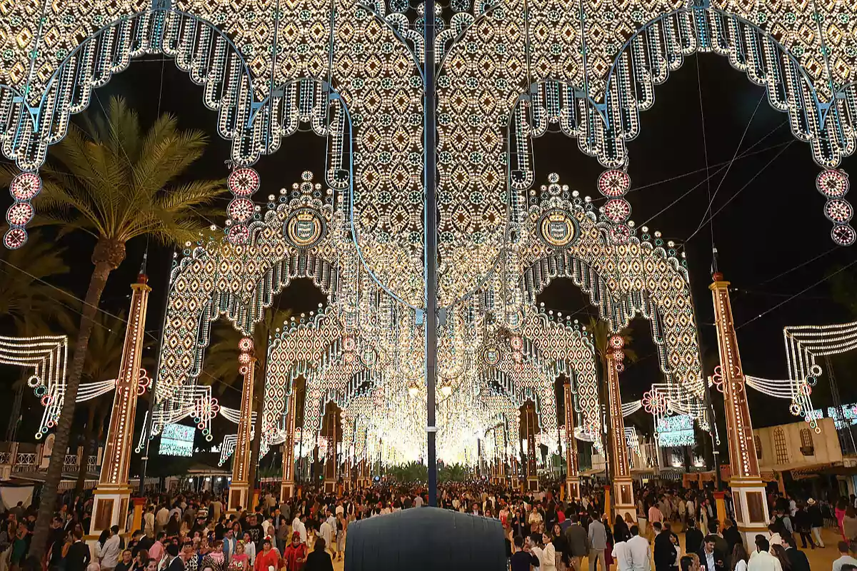 Una multitud de personas camina bajo un impresionante arco de luces decorativas en un evento nocturno al aire libre.