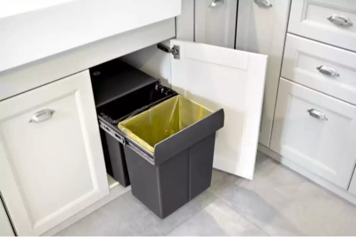 Un contenedor de basura extraíble con dos compartimentos en un gabinete de cocina blanco. Un contenedor de basura extraíble con dos compartimentos en un gabinete de cocina blanco.