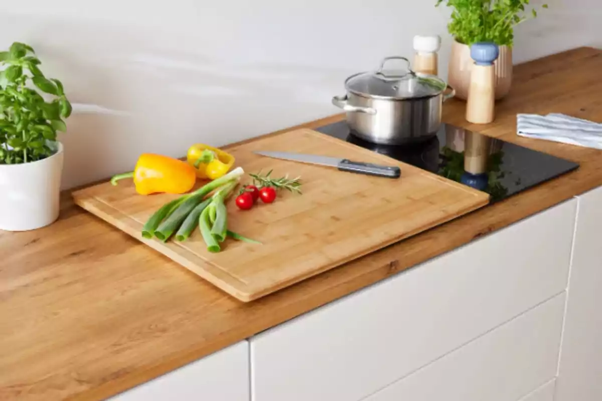Encimera de cocina con tabla de cortar, cuchillo, verduras frescas y una olla sobre una estufa. Encimera de cocina con tabla de cortar, cuchillo, verduras frescas y una olla sobre una estufa.