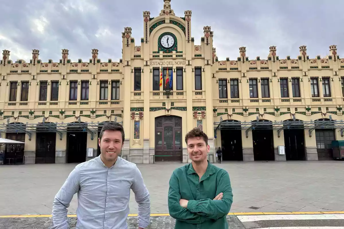 Dos personas posan frente a un edificio histórico con un reloj en la parte superior.