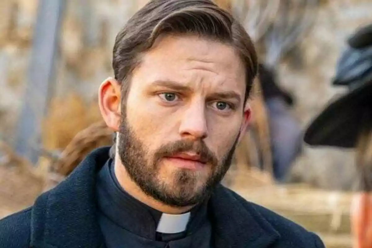 Imagen del actor Daniel Schröder con barba y cabello corto vestido con sotana negra y alzacuellos blanco mirando hacia el frente con expresión seria. Imagen del actor Daniel Schröder con barba y cabello corto vestido con sotana negra y alzacuellos blanco mirando hacia el frente con expresión seria.