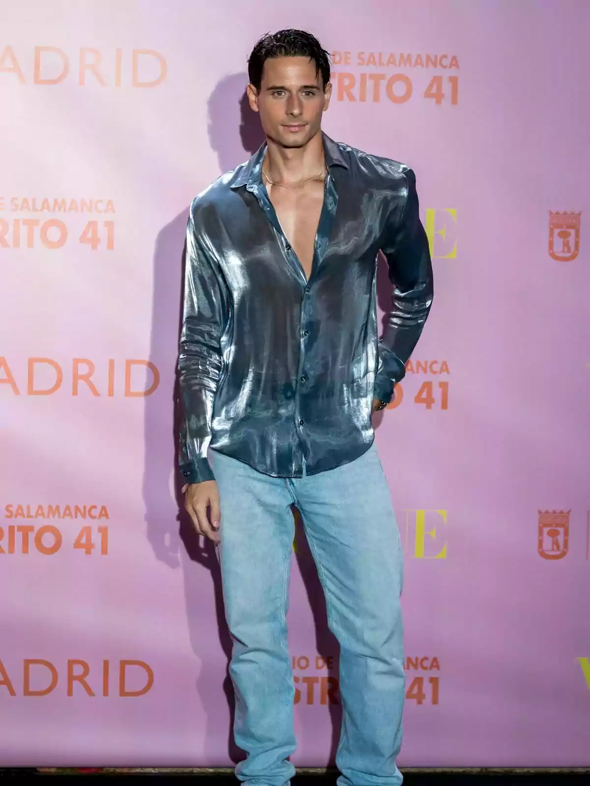 David Matarín posando con camisa brillante y jeans frente a un fondo rosa con texto.