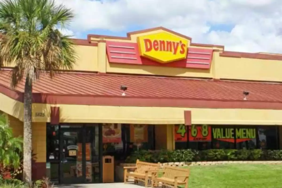 Facade of a Denny's restaurant with a yellow and red sign and an outdoor seating area surrounded by greenery. Facade of a Denny's restaurant with a yellow and red sign and an outdoor seating area surrounded by greenery.