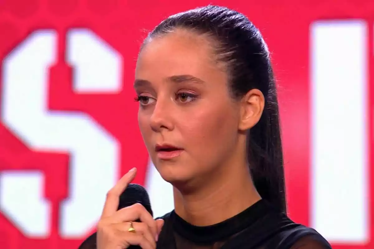 Victoria Federica con cabello oscuro recogido sostiene un micrófono frente a un fondo rojo en El Desafío. Victoria Federica con cabello oscuro recogido sostiene un micrófono frente a un fondo rojo en El Desafío.