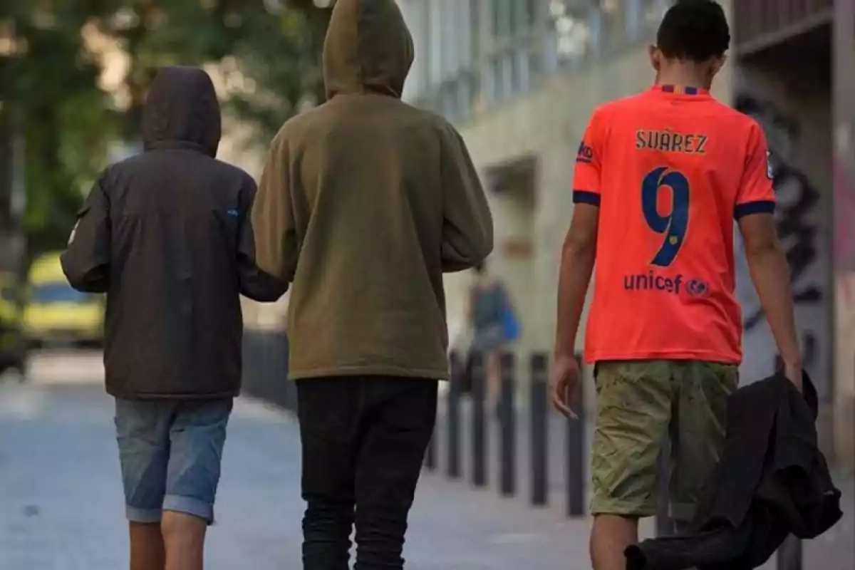 Tres personas caminando por una calle, dos con sudaderas con capucha y una con una camiseta de fútbol.