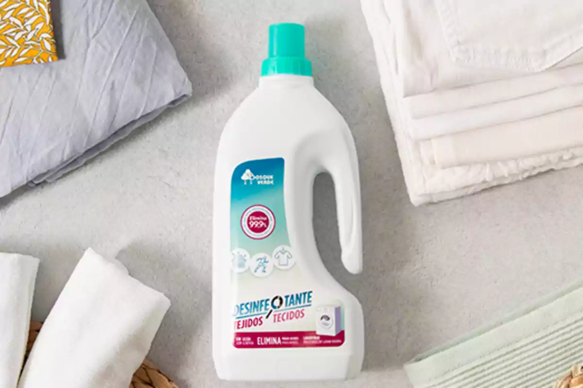 Botella de desinfectante de tejidos sobre una superficie junto a ropa doblada. Botella de desinfectante de tejidos sobre una superficie junto a ropa doblada.