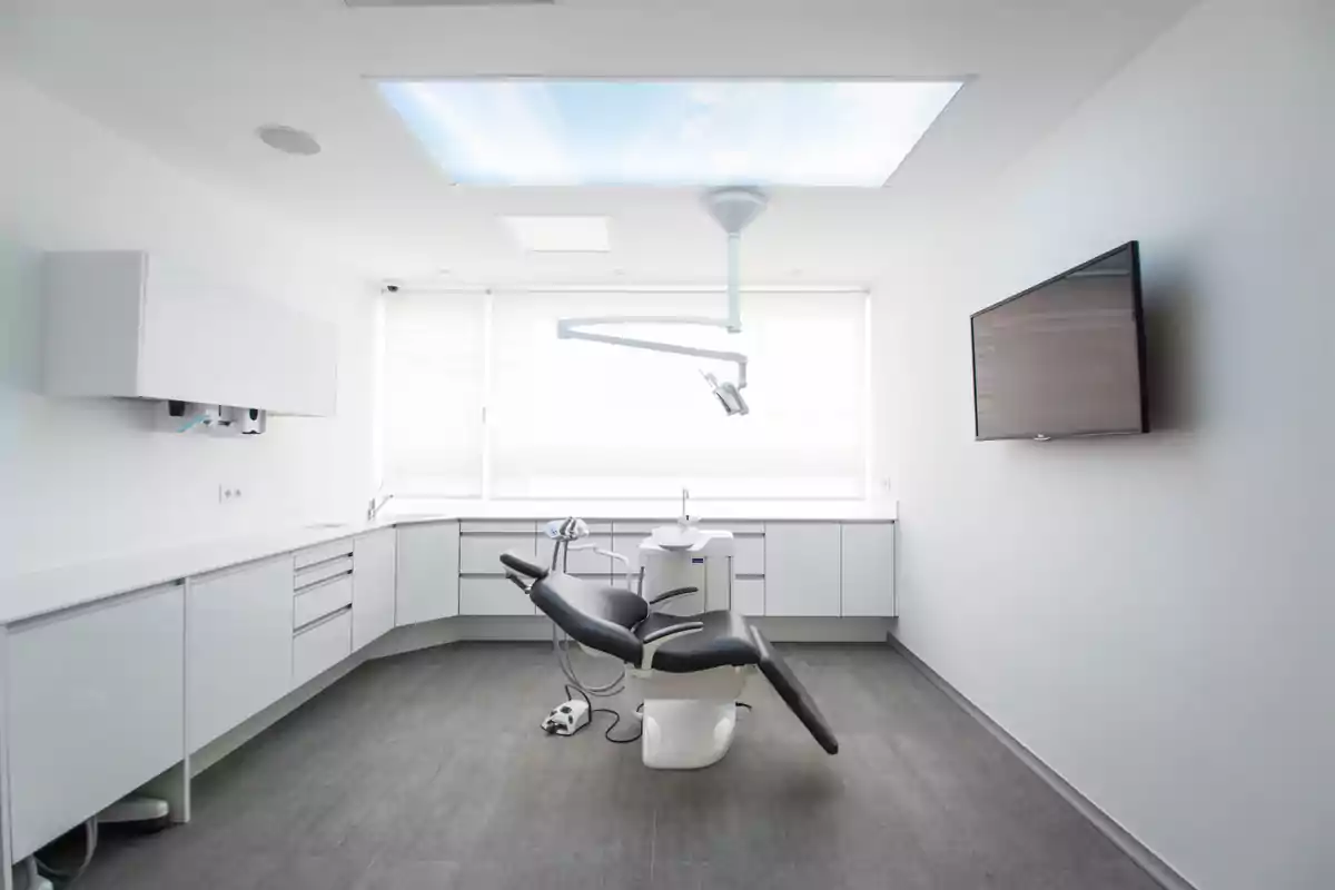 Consultorio dental moderno con silla de dentista, luz de techo y pantalla en la pared.