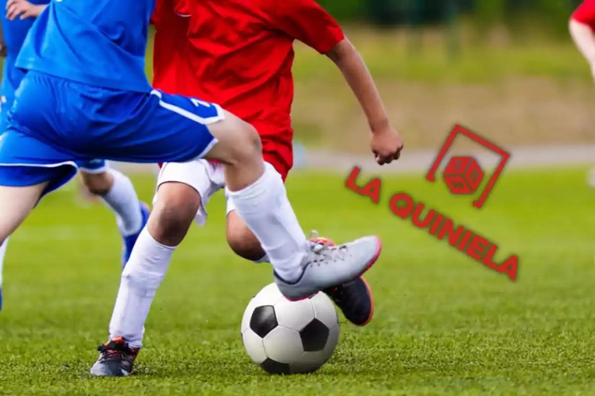 Jugadores de fútbol en acción disputando el balón en un campo de juego con el logo de "La Quiniela" en la esquina derecha.